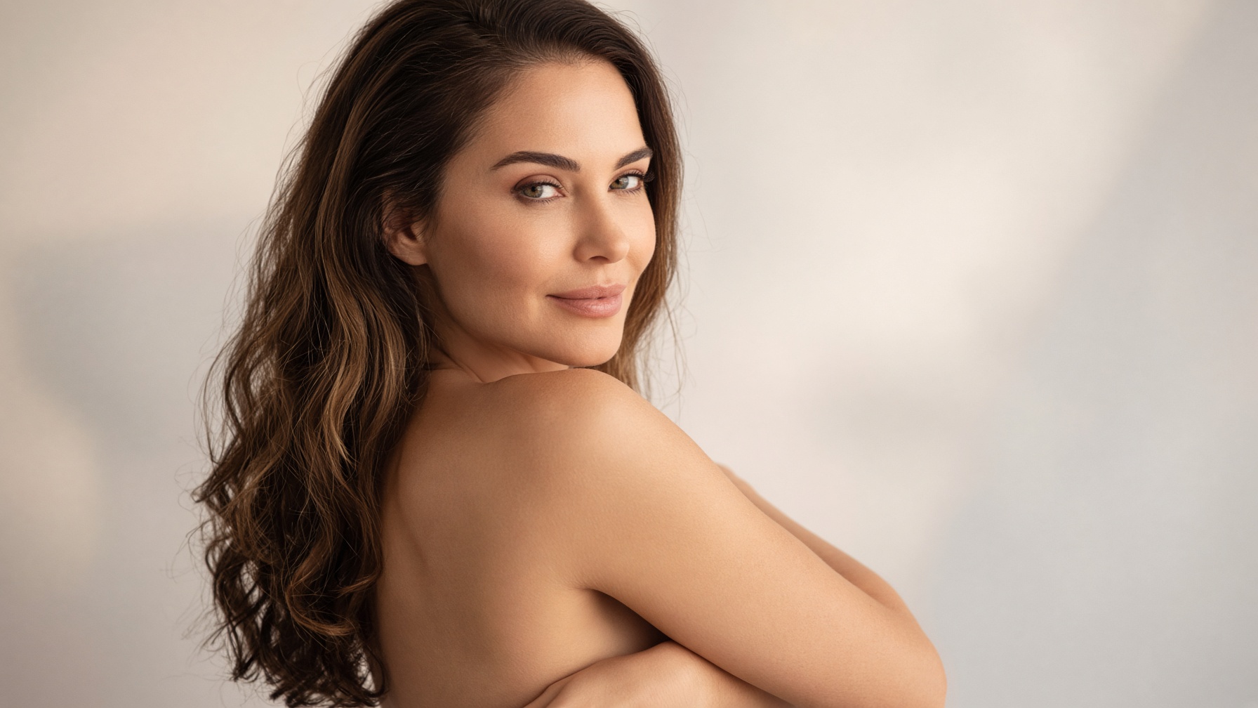 Editorial portrait — quiet confidence, bare shoulder, looking back toward the camera.